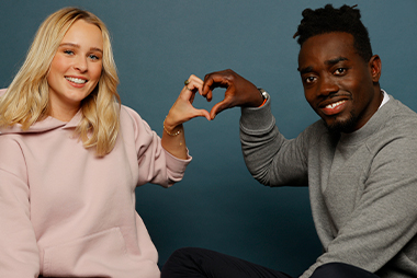 Zwei Personen formen mit ihren Händen gemeinsam ein Herz vor einem blauen Hintergrund.