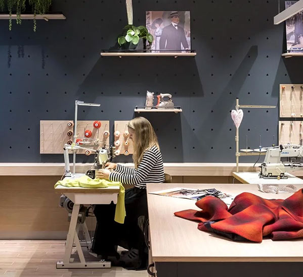 Eine Frau arbeitet an einer Nähmaschine in einem Atelier mit Stoffen und Nähzubehör um sie herum.