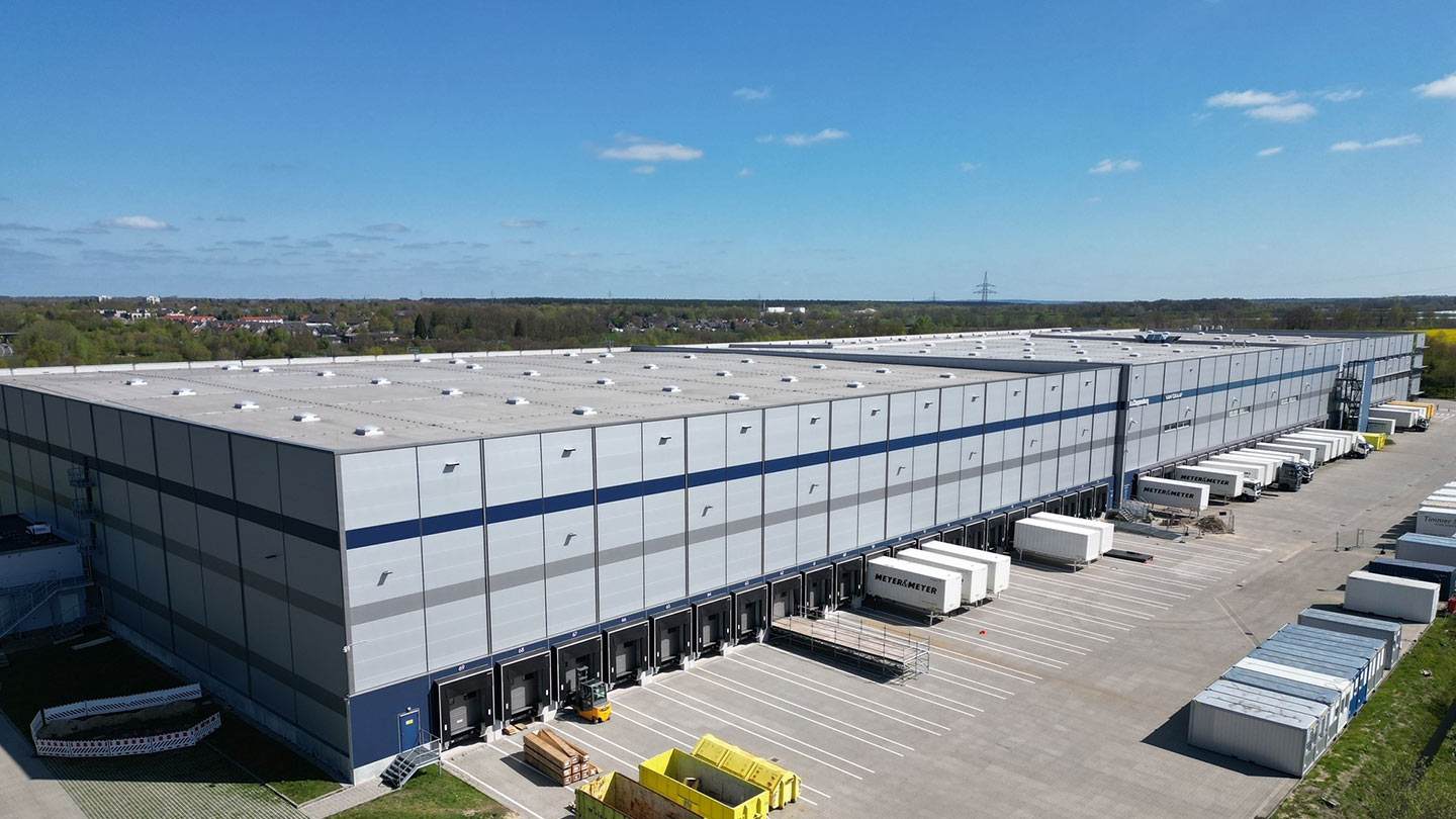 Ein großes Logistikzentrum mit zahlreichen Verladerampen und weißen Anhängern, umgeben von Wiesen und einem klaren Himmel.