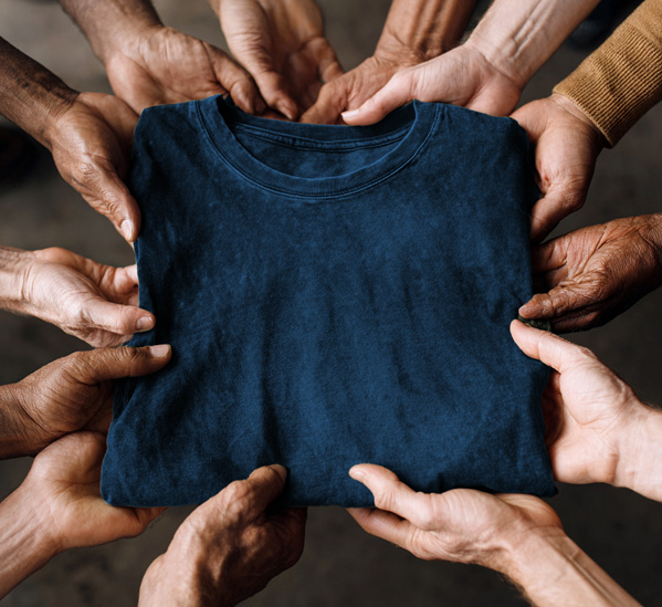 Mehrere Hände unterschiedlicher Hauttöne halten gemeinsam ein dunkelblaues T-Shirt.