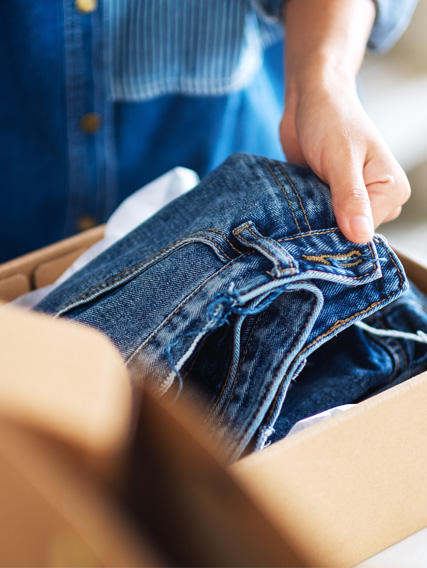 umwelt_topic_slider_retouren_427x568 Eine Person packt eine blaue Jeans aus einem Karton aus.